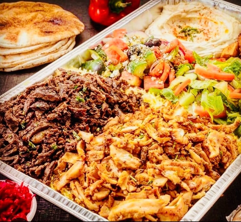 Large platter with beef and chicken shawarma, hummus, salads, and pita bread.