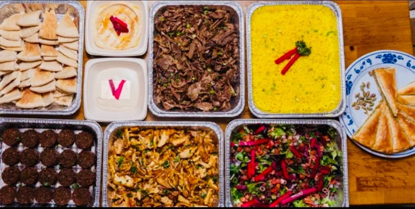 A catering spread of Middle Eastern food including pita, hummus, falafel, rice, meat, and salad.