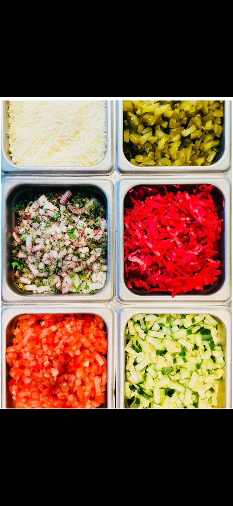 Six metal containers filled with various chopped ingredients like cheese, pickles, onions, cabbage, tomatoes, and cucumbers.